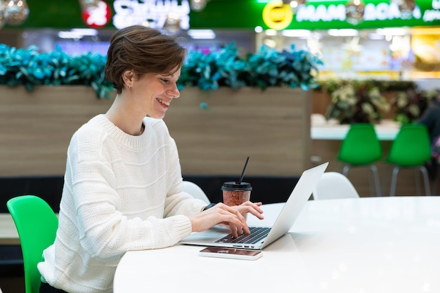 Foto einer jungen positiven Frau, die im Food Court eines Einkaufszentrums an einem Tisch sitzt und arbeitet