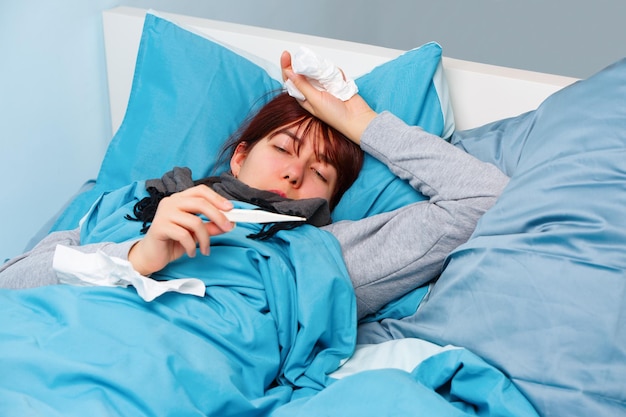 Foto einer kranken Frau mit Thermometer, die auf dem Bett liegt
