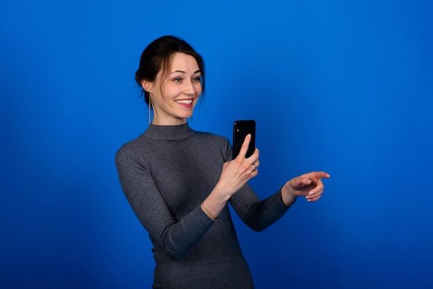 Foto einer lächelnden, fröhlichen jungen Frau im grauen Kleid auf blauem Hintergrund