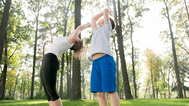 Foto einer Mutter mittleren Alters mit ihrem Kind im Teenageralter, die Yoga und Atemübungen im Park macht. Familie, die sich beim Sport um ihre geistige und körperliche Gesundheit kümmert