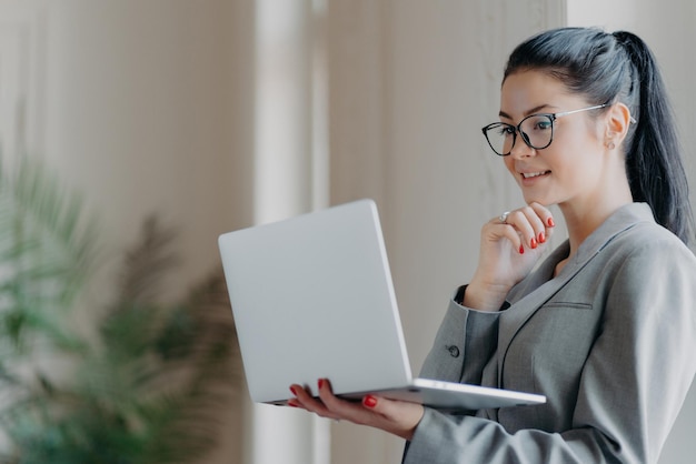 Foto einer schönen brünetten Frau, die ihr Kinn konzentriert auf den Laptop-Bildschirm hält, studiert den Finanzmarkt und konzentriert sich auf einen Remote-Job und bereitet eine Veröffentlichung vor. Freelacer schaut sich ein Webinar an, um seine Fähigkeiten zu verbessern