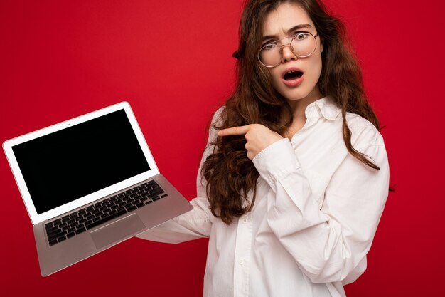 Foto einer schönen jungen Frau, die einen Computer-Laptop hält und in die Kamera schaut, isoliert über bunt