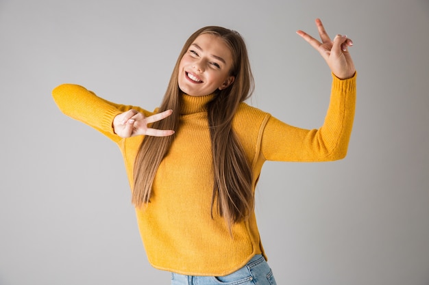 Foto einer schönen jungen glücklichen Frau lokalisiert über graue Wand, die Friedensgeste zeigt.