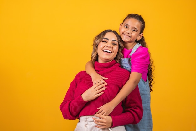 Foto einer schönen jungen Mama, die ihre Arme umarmt und ihre kleine Tochter umarmt, gute Laune entzückende aufrichtige Herzgefühle in den hinteren Jeans-T-Shirts isoliert mit gelbem Farbhintergrund