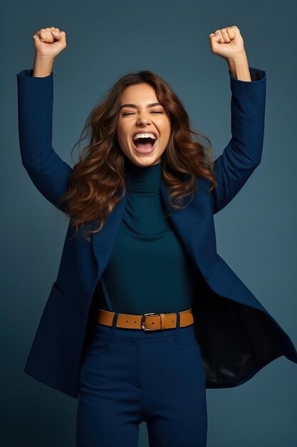 Foto einer überglückten, fröhlichen Frau in stilvollen Kleidern, die den Erfolg feiert, die Hände hebt, die Fäuste auf einem dunkelblauen Hintergrund isoliert