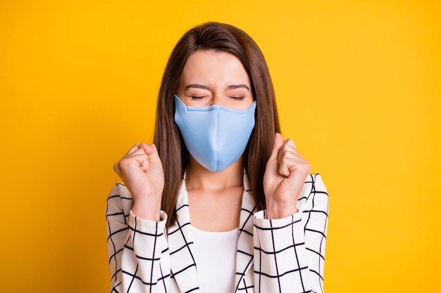 Foto einer überraschten Geschäftsfrau, die eine blaue Gesichtsmaske mit Fäusten und geschlossenen Augen trägt, isoliert gelber Farbhintergrund