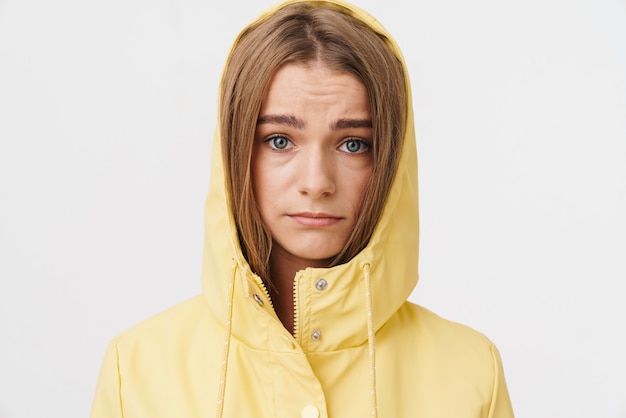 Foto einer unglücklichen kaukasischen Frau im Regenmantel, die posiert und in die Kamera schaut