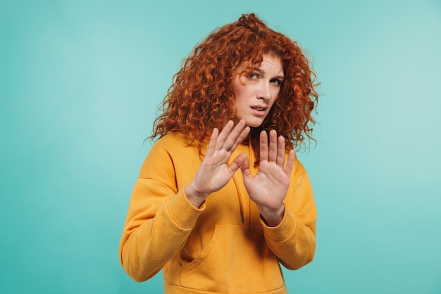 Foto einer unzufriedenen Frau der 20er Jahre mit lockigem Ingwerhaar, die eine Stopp-Geste macht und die Ablehnung einzeln über der blauen Wand ausdrückt?