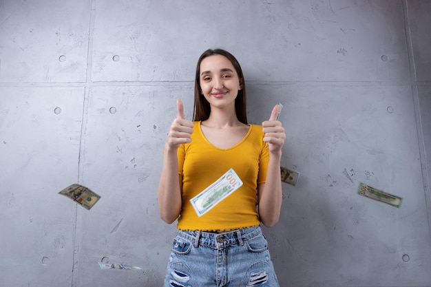 Foto einer wohlhabenden Frau in einfacher Kleidung, die einen Fan von Dollargeld hält, isoliert vor einem Betonwandhintergrund