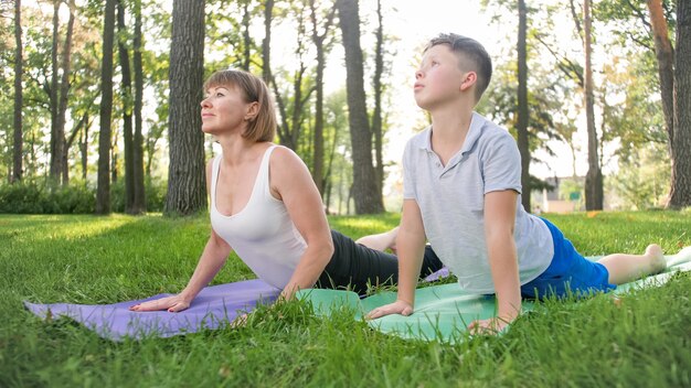 Foto einer Yogalehrerin mittleren Alters oder eines Guru, der Teenager beim Yoga unterrichtet. Frau mit Junge meditiert und streckt sich auf Gras im Park