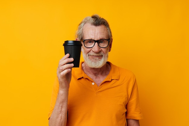 Foto eines alten Mannes im Ruhestand in einem gelben T-Shirt ein Glas mit einem Getränk isolierter Hintergrund