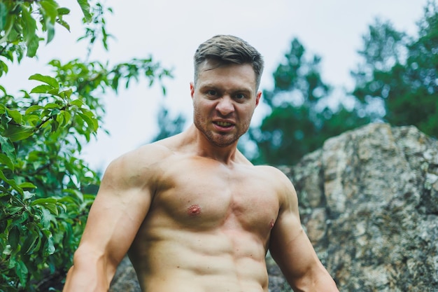 Foto eines Athleten, eines muskulösen, athletischen jungen Mannes, der mit einem nackten Rumpf in den Waldbergen Übungen macht