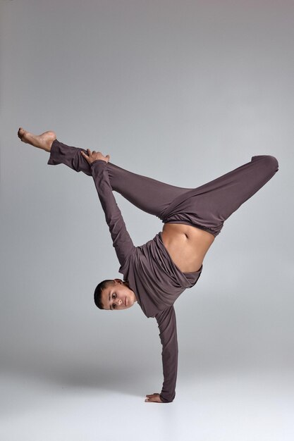 Foto eines athletischen Balletttänzers, der in einem grauen Trainingsanzug gekleidet ist und ein Tanzelement vor grauem Hintergrund im Studio macht.