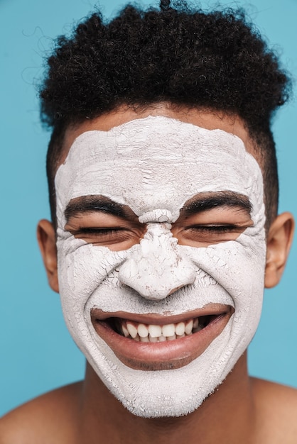 Foto eines aufgeregten Afroamerikaners in kosmetischer Gesichtsmaske, der isoliert auf Blau lächelt