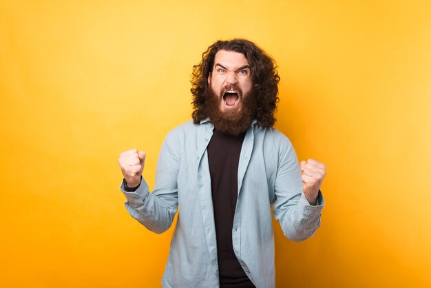 Foto eines bärtigen Hipster-Mannes, der über gelbem Hintergrund feiert und schreit