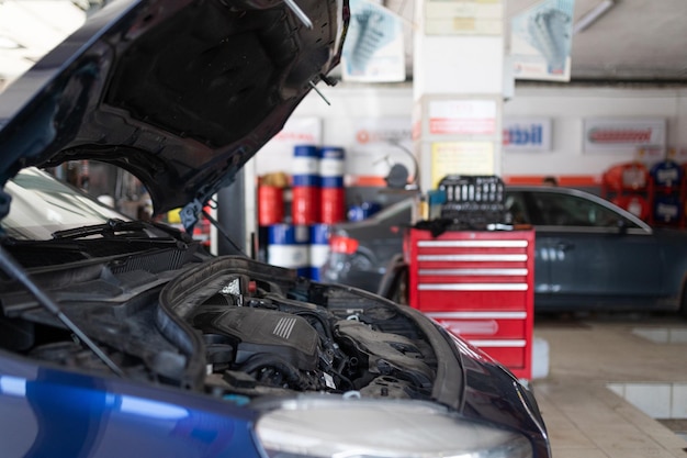 Foto eines blauen Pkw an der Tankstelle, der mit offener Haube repariert wird