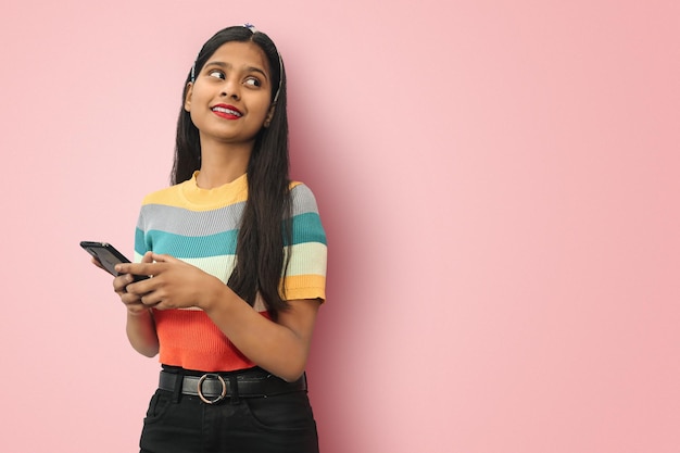 Foto eines fröhlichen, süßen, attraktiven indischen asiatischen Mädchens, das ein Telefon mit Händen hält, die zahnhaft lächeln und auf die andere Seite schauen, mit Mock-up-Platz, um Text zu schreiben