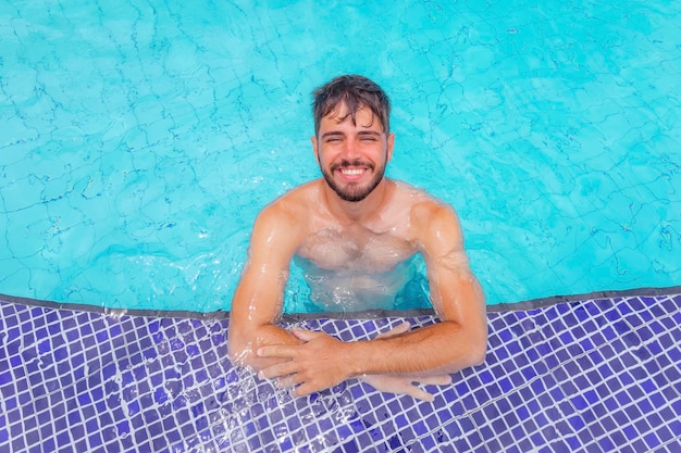 Foto eines gutaussehenden Mannes, der am Swimmingpool in der Sommerlandschaft lächelt