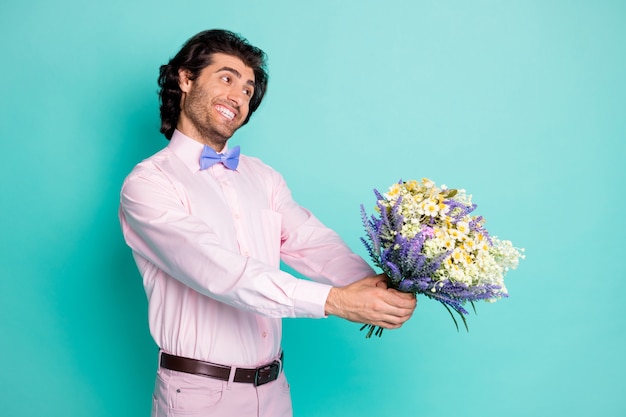 Foto eines gutaussehenden, strahlenden, sanften Mannes in rosafarbenem Outfit, der Ihnen zum Geburtstag gratuliert und Blumenstrauß präsentiert, sehen leer aus, Arme isoliert blaugrüner Hintergrund