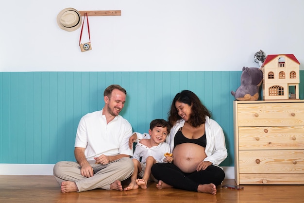 Foto eines jungen, fröhlichen, positiv lächelnden Paares, schwangere Frau und Ehemann mit ihrem Sohn, der sich zu Hause entspannt