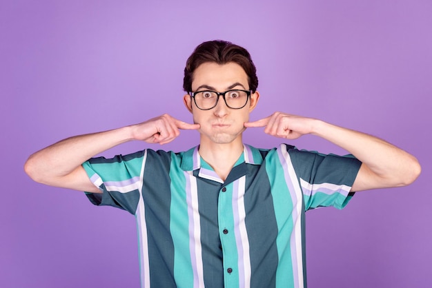 Foto eines jungen Mannes, der den Atem anhält, berührt die Finger, schmollte Wangen und verzog das Gesicht isoliert über violettem Hintergrund