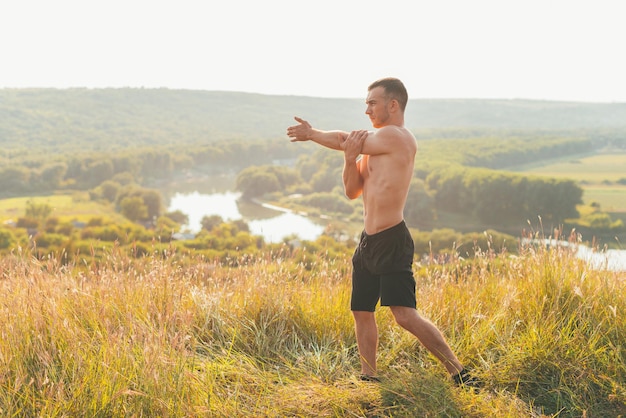 Foto eines jungen Sportlers, der sich bei Sonnenuntergang im Freien aufwärmt