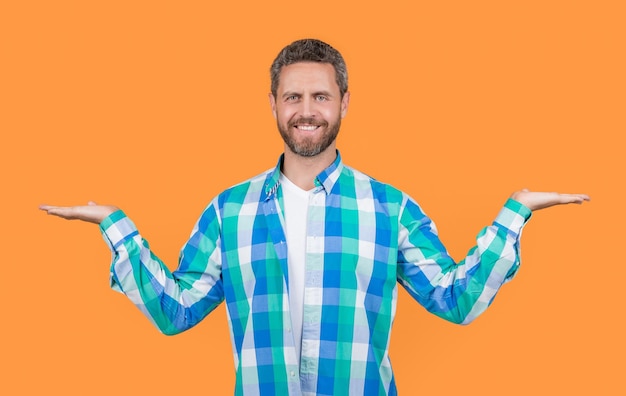 Foto eines kaukasischen Mannes in kariertem Hemd, der einen kaukasischen Mann im lässigen Stil präsentiert. bärtiger kaukasischer Mann in lässigem Hemd isoliert auf gelbem Hintergrund. Kaukasischer legerer Mann im Studio