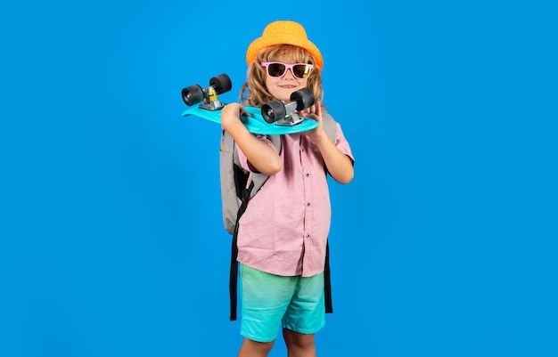 Foto eines kleinen Jungen, der ein Skateboard isoliert auf blauem Hintergrund hält. Lässige Kultur. Kind mit