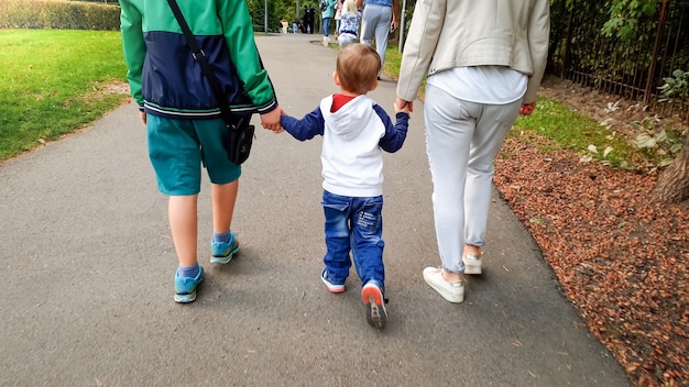 Foto eines kleinen Kleinkindjungen, der seine Mutter und seinen älteren Bruder mit der Hand hält und im Herbstpark spazieren geht