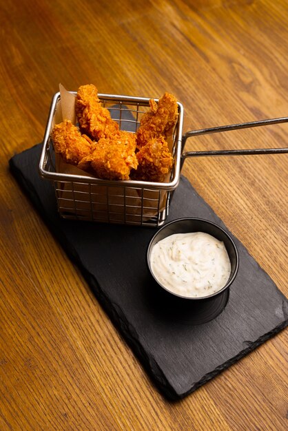 Foto eines kleinen Metallkorbs voller Finger oder Nuggets und einer kleinen Schüssel mit Soße.