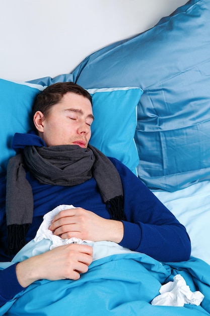 Foto eines kranken Mannes mit Schal und Taschentüchern, der im Bett liegt