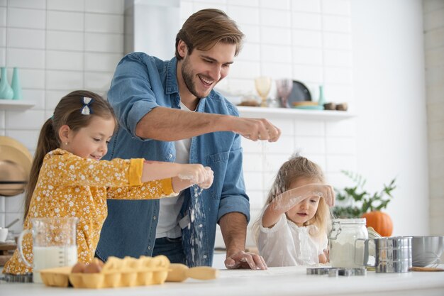 Foto eines lächelnden Vaters und der Töchter, die in der Küche backen und Spaß haben.