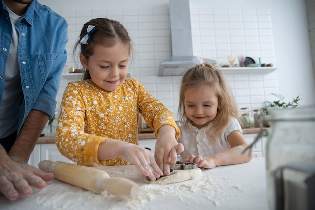 Foto eines lächelnden Vaters und der Töchter, die in der Küche backen und Spaß haben.