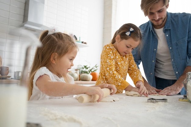 Foto eines lächelnden Vaters und der Töchter, die in der Küche backen und Spaß haben.