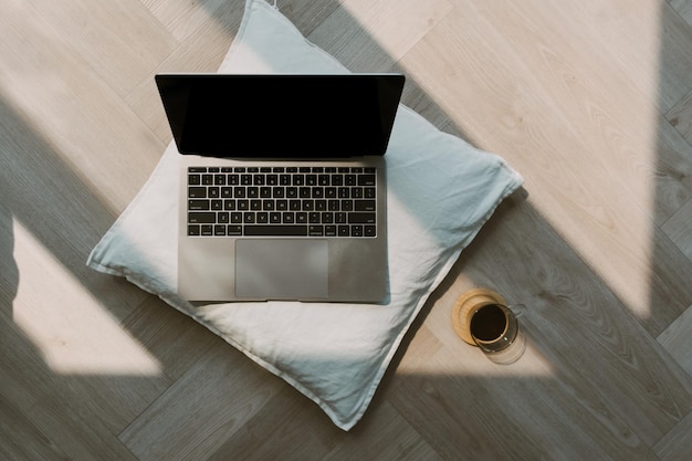 Foto eines Laptops, das einen schwarzen leeren Bildschirm zeigt und ein weißes Kissen auf dem Holzboden in einem gemütlichen Zimmer mit