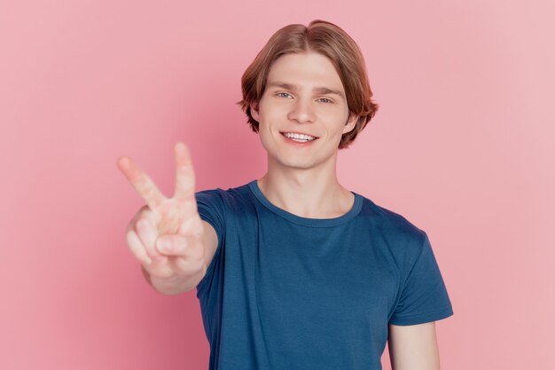Foto eines lustigen beeindruckten jungen Mannes, der glückliches positives Lächeln zeigt, das V-Zeichen coolen Frieden zeigt, isoliert rosa Farbhintergrund