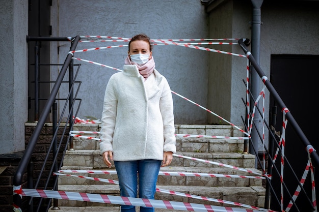 Foto eines Mädchens in einer Maske, das mit Gefahrenwarnbändern auf der Straße steht