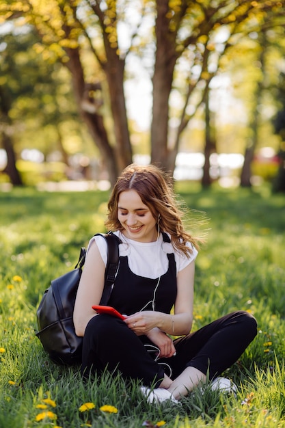 Foto eines positiven fröhlichen Teenager-Mädchens verbringt Zeit im Park und mit Handy.