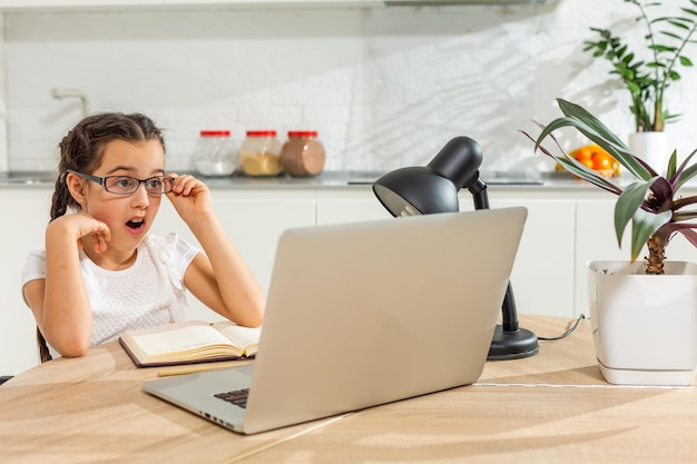 Foto eines positiven Kindermädchens, das einen Remote-Sitz-Schreibtisch-Tisch mit einem Laptop studiert, hat eine Online-Kommunikationsstunde mit einem Tutor, der einen Bericht im Haus schreibt