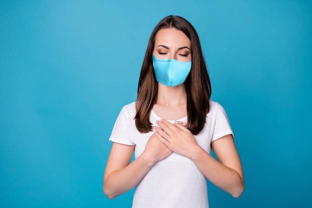 Foto eines ruhigen friedlichen Mädchens, das die Hände auf die Brust legt, die Ruhe bewundern, sich entspannen, die Covid-Infektion im Gesundheitswesen Schutz tragen medizinische Maske Freizeitkleidung isoliert blauer Hintergrund