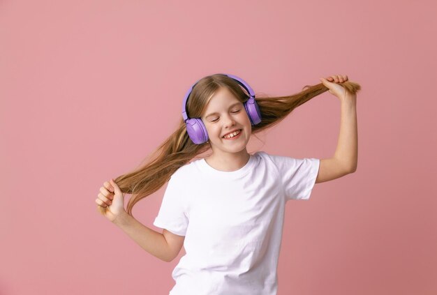 Foto eines süßen, lustigen jungen Mädchens im Teenageralter in einem rosa Pullover, der tanzt und Musik auf einem Hintergrund genießt