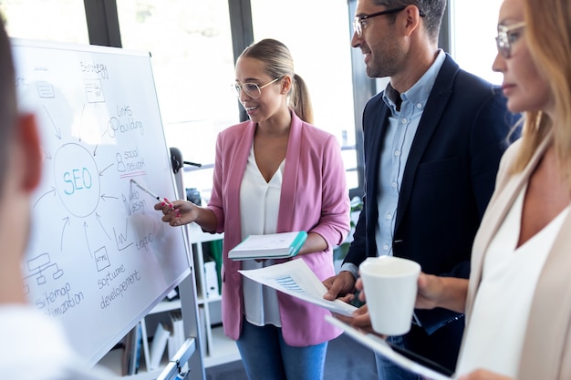 Foto foto de elegante joven empresaria apuntando a la pizarra blanca y explicar un proyecto a sus colegas en el lugar de coworking.