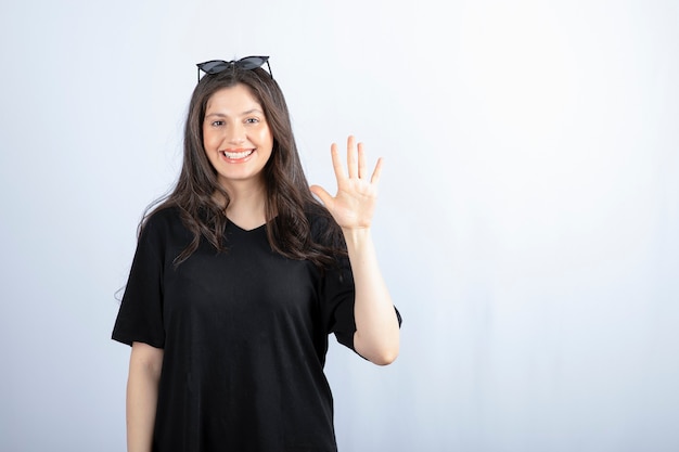 Foto de elegante mujer joven sonriente posando con gafas de sol y mostrando el número cinco con la mano.