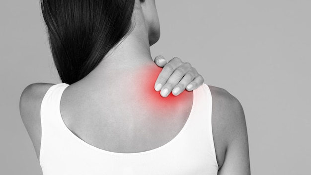 Foto em preto e branco de mulher com forte dor nas costas massageando o ombro e tocando a zona vermelha inflamada