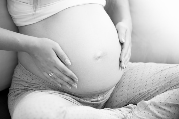 Foto em preto e branco do close up de uma mulher grávida segurando as mãos na barriga