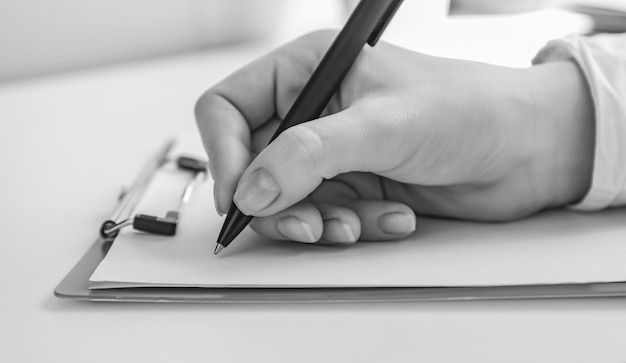 Foto em preto e branco Foco em uma mão feminina segurando uma caneta pronta para escrever algo em um pedaço de papel em branco folha branca