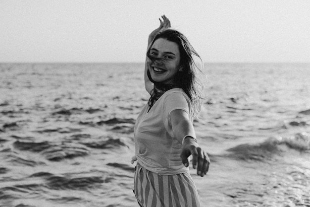 Foto em preto e branco Jovem feliz dançando girando pelo mar em um vestido amarelo esvoaçante
