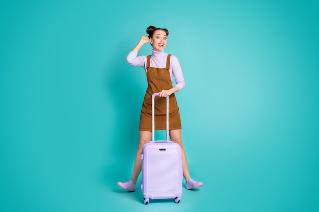 Foto em tamanho grande de atraente alegre engraçado bonito senhora turista esperando registro de avião ouvir nome segurar mala usar vestido marrom sapatos de pulôver roxo isolado cor de fundo verde-azulado