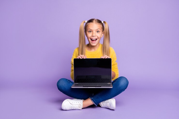 Foto foto em tamanho grande de criança espantada e animada mostra laptop mostra tela sensível ao toque grito uau omg sente-se pernas cruzadas e dobradas, use roupa de estilo casual isolada sobre parede de cor violeta