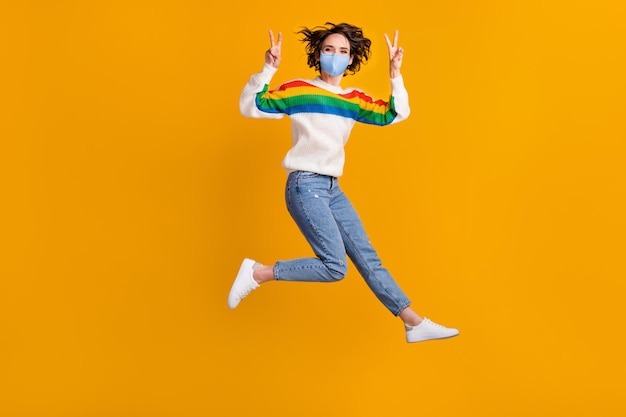 Foto em tamanho grande de mulher engraçada salto show v-sign usar máscara suéter calça jeans isolado em fundo amarelo